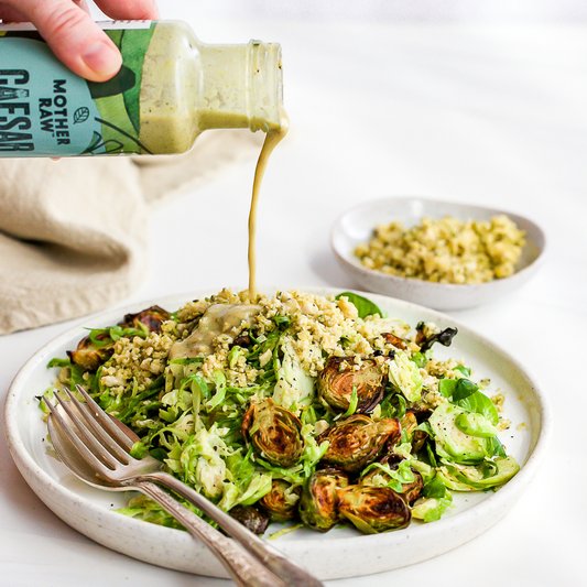 Caesar Dressing being poured on brussel sprout salad.